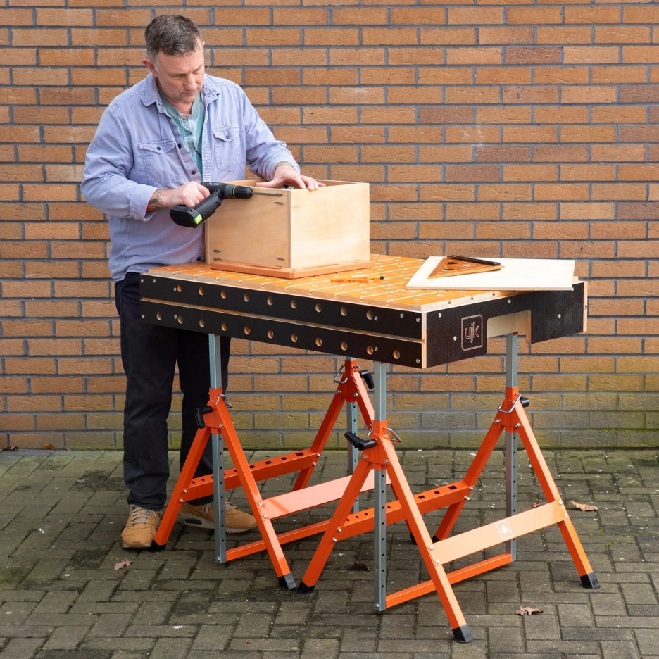 Man working on a wooden box on UJK Tools Trestle  outdoors against a brick wall.