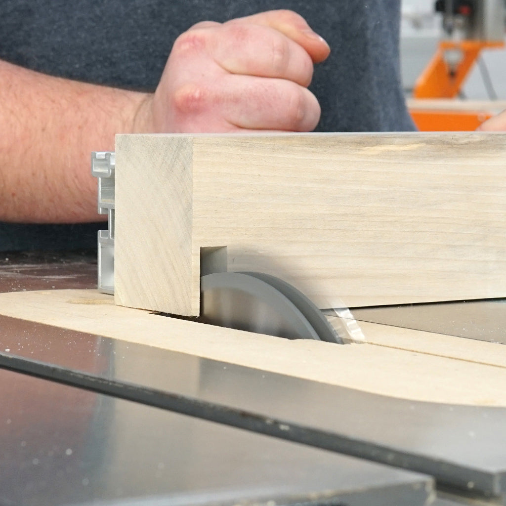 A worker mills a wide dado in a large piece of solid wood on a table saw with mitre gauge with Amana Tool 12T dado set.