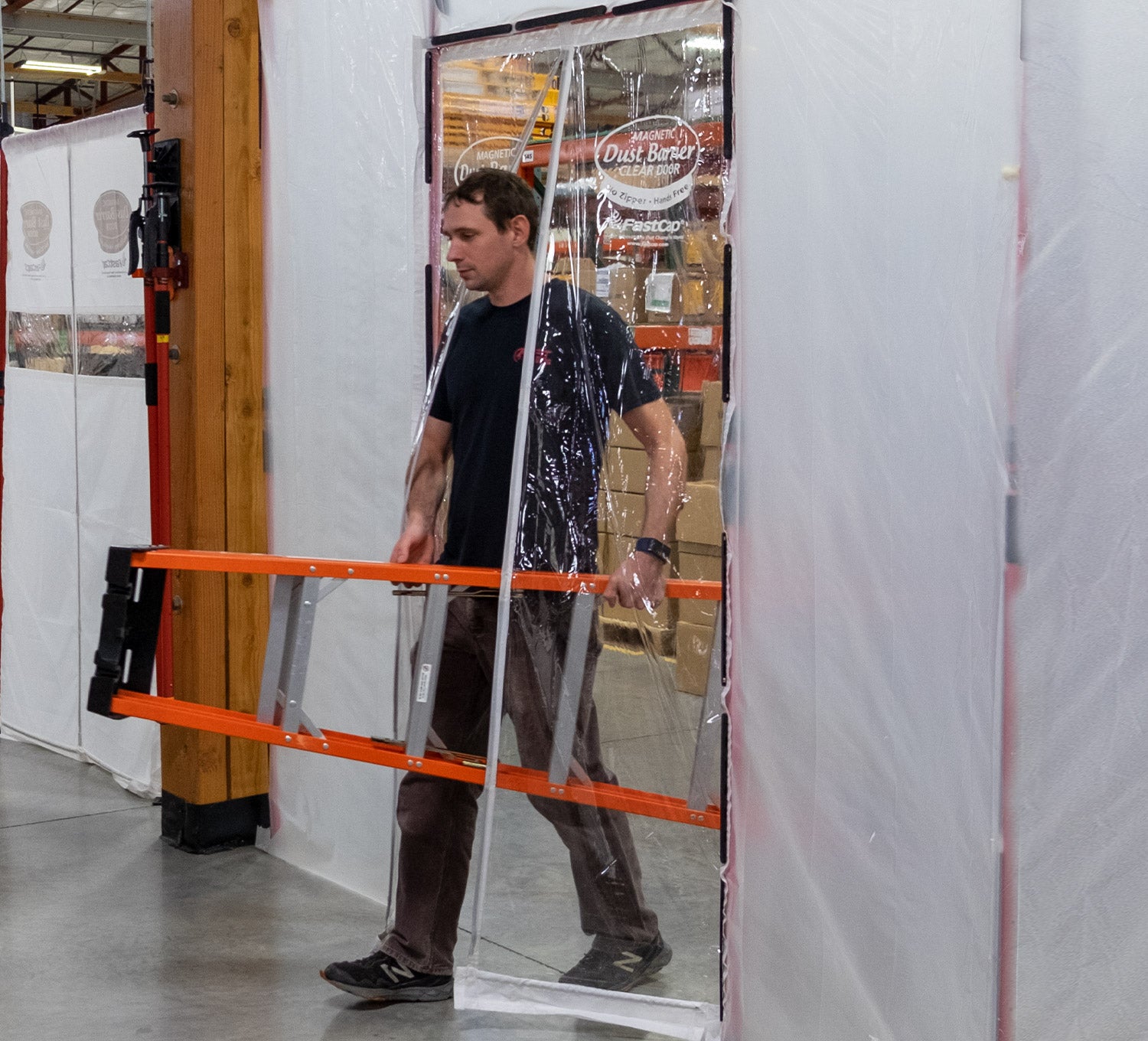 A worker carries a long ladder through a hands-free clear magnetic dust barrier door, which opens automatically for him.