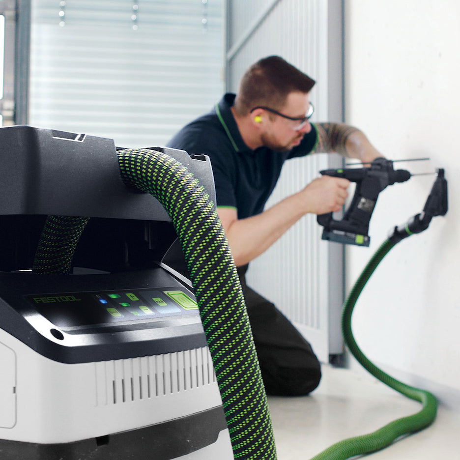 Worker uses a Festool CTC MIDI I Dust Extractor connected dust extraction attachment while using hammer drill.