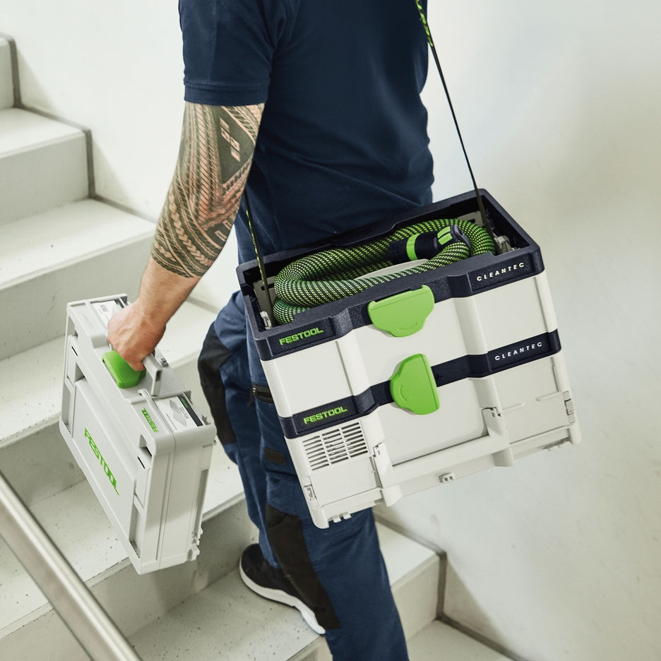 Man carries CTC SYS Dust Extractor with strap on his shoulder up stairs while carrying another Systainer.