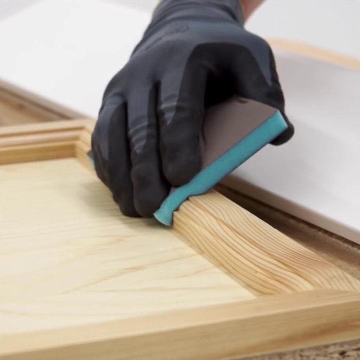 A gloved hand uses an abrasive sponge to sand a routed classical moulding profile.
