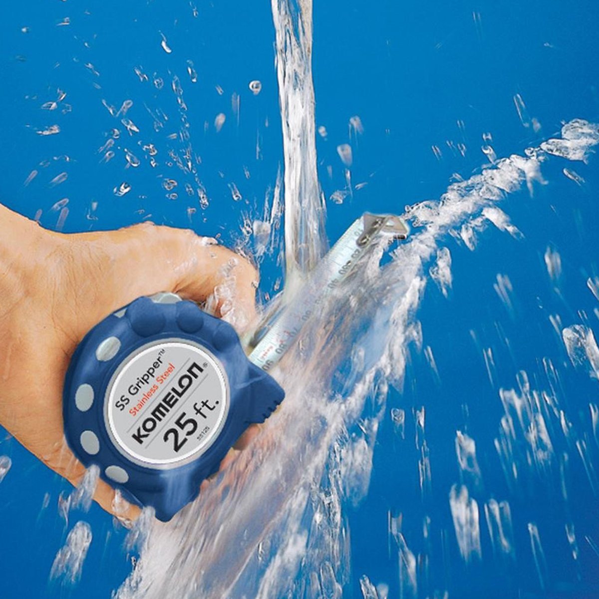 A user holds a Komelon Stainless Steel Gripper 25 foot tape measure under stream of water to wash it out.