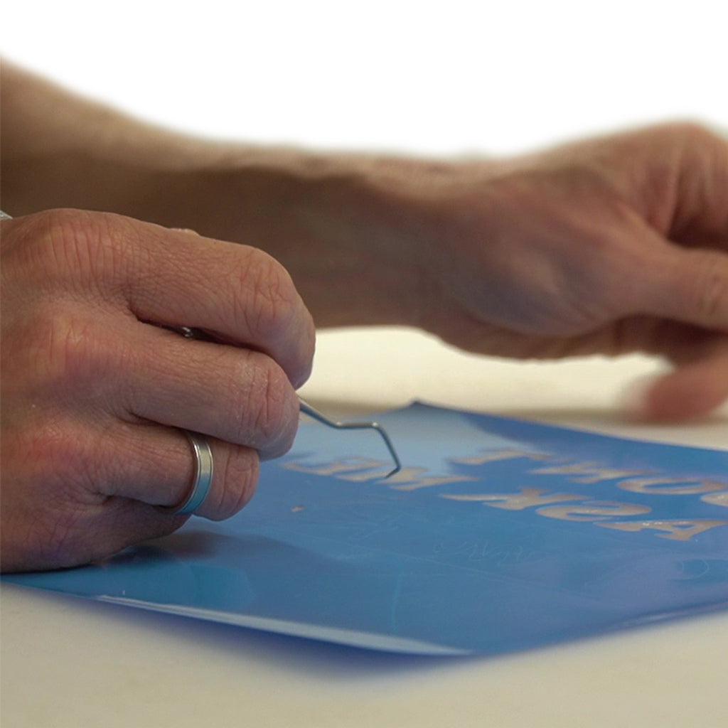 An artist uses a weeding tool to carefully remove a small part of vinyl decal.