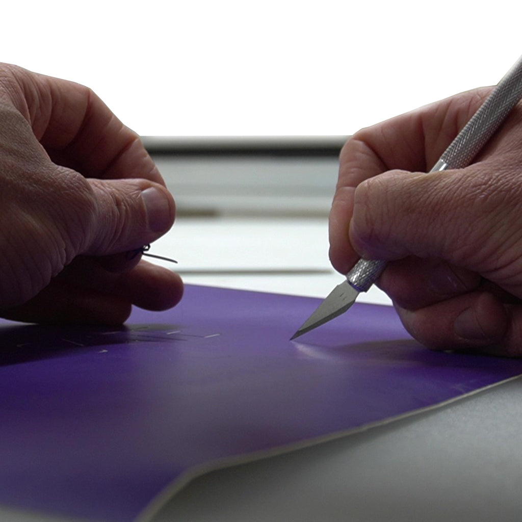 An artist uses a craft knife to carefully cut a section of vinyl decal.